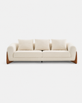 A modern three-seat sofa upholstered in warm off-white fabric with three matching back cushions and angled wooden legs, shown against a plain light gray background.