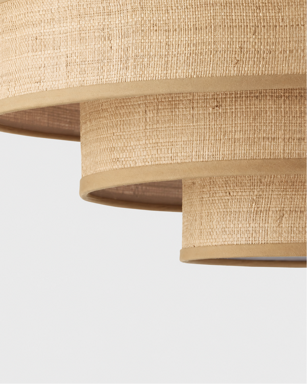 Close-up of a tiered ceiling light fixture with woven natural fiber shades in a warm beige color, set against a plain light gray background.