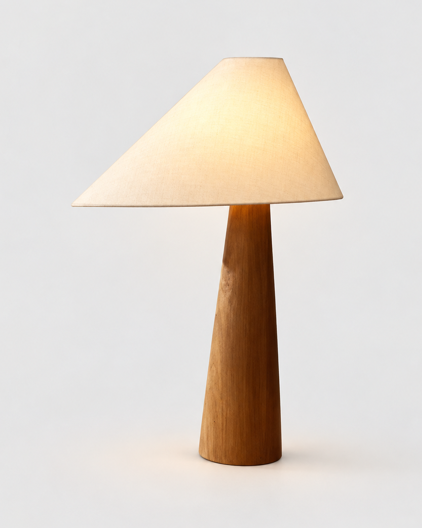 A modern table lamp with a tapered wooden base and a conical fabric shade, glowing with a warm light against a neutral light gray background.